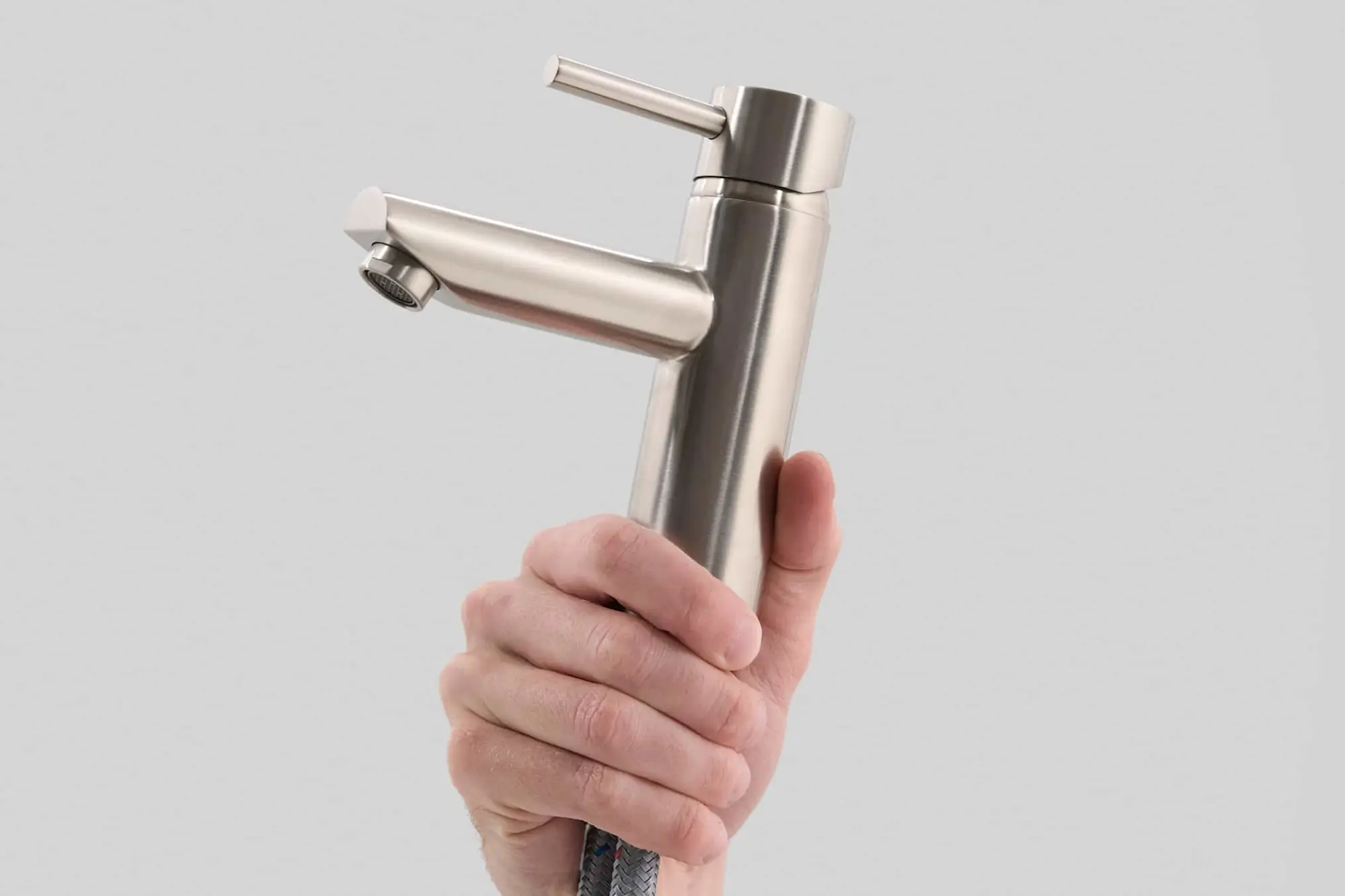 Hand holding a brushed nickel bathroom faucet with single lever handle against a gray background.