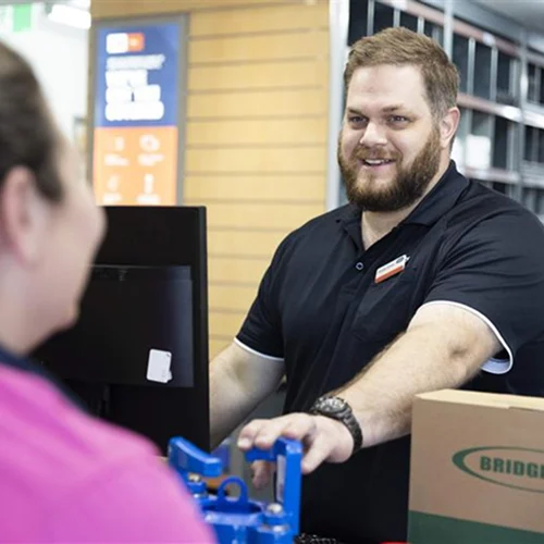 Staff member in Reece uniform working at a counter with a computer and blue mechanical part on display.