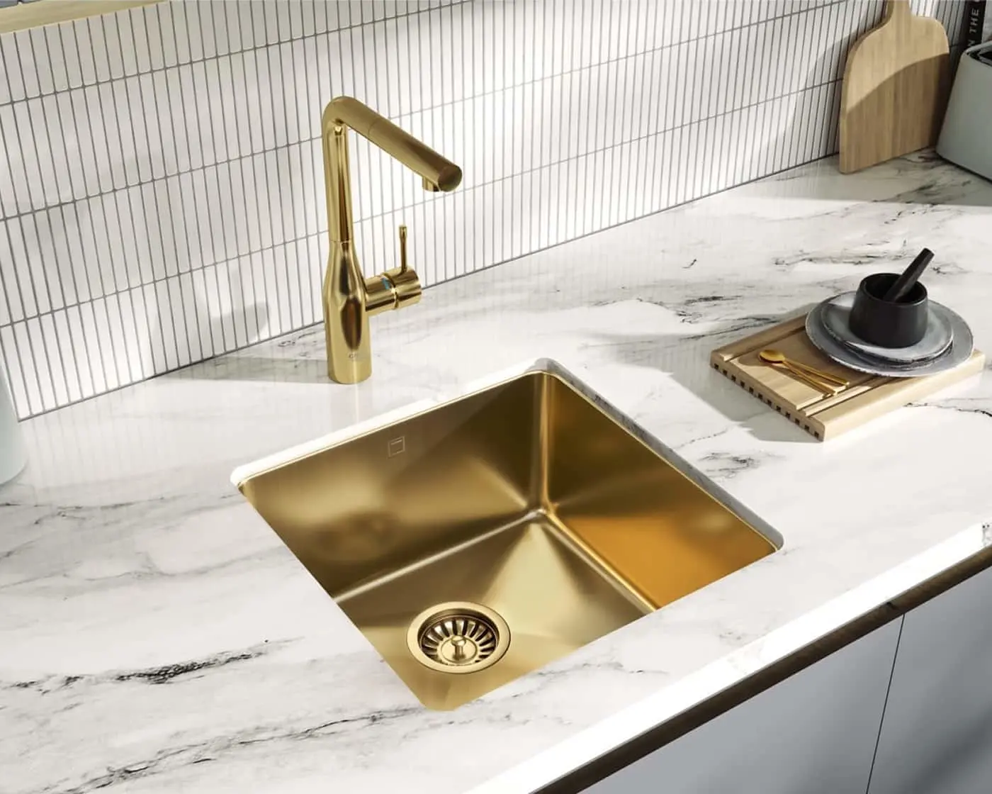 Modern kitchen with gold sink and faucet on white marble countertop, white tile backsplash, and wooden accessories.