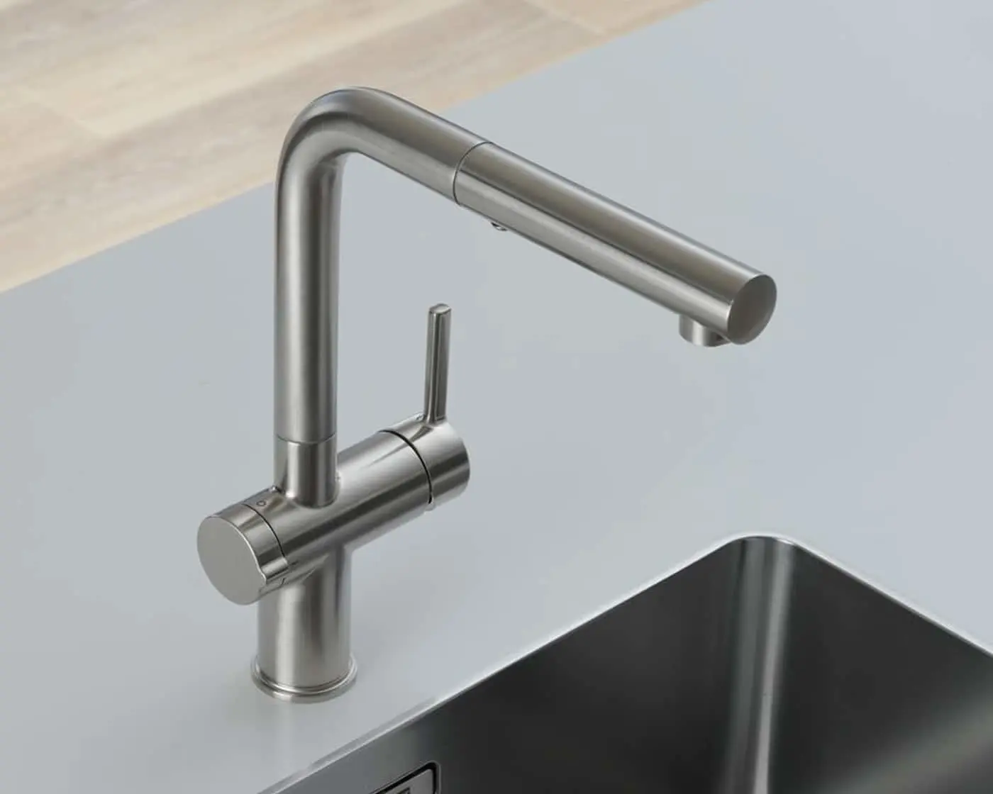 Modern stainless steel kitchen faucet with L-shaped spout mounted on a light countertop above a dark sink.