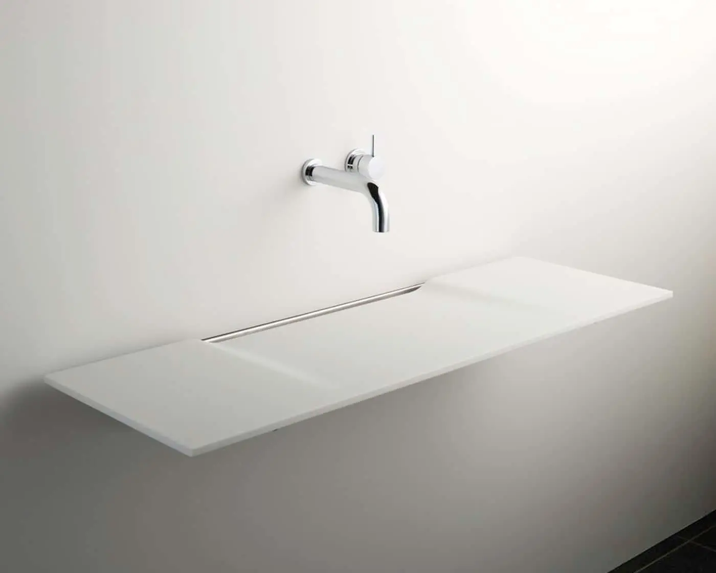 Minimalist white bathroom sink with wall-mounted chrome faucet against a light gray wall in a modern design.
