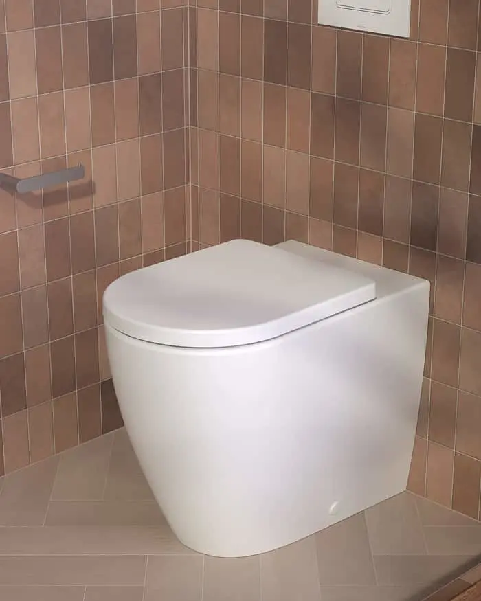 Modern white wall-mounted toilet with closed lid in bathroom with brown tiled walls and flush button above.