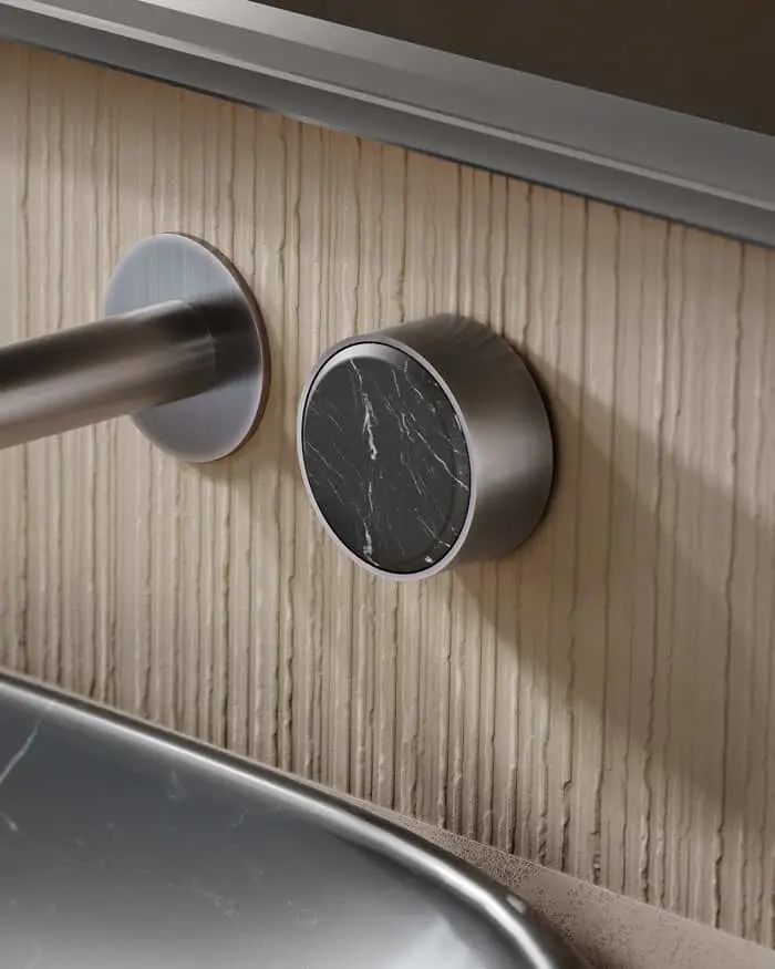 Modern bathroom fixture with metal outlet and circular black marble control knob mounted on light wood paneling.