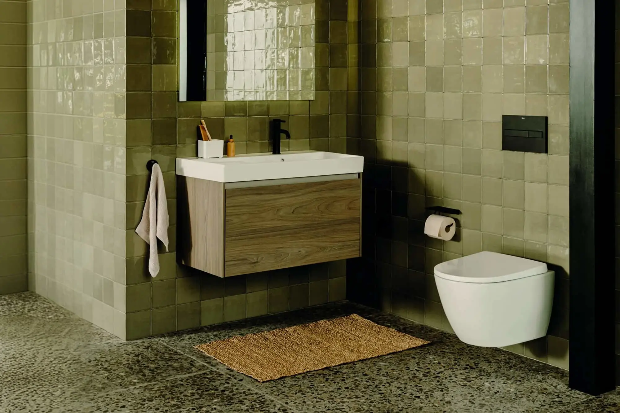 Modern bathroom with green tile walls, wall-mounted vanity with wood cabinet, white toilet, and terrazzo floor.
