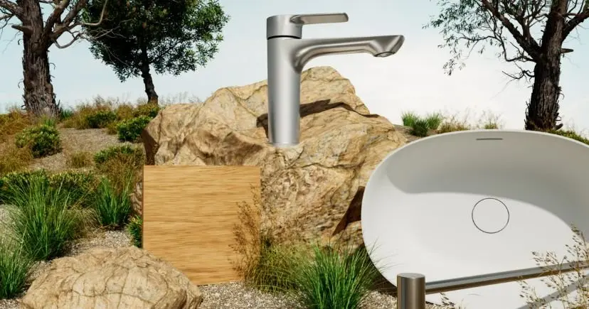 Modern silver bathroom faucet and white sink basin displayed outdoors against natural rock and vegetation backdrop.