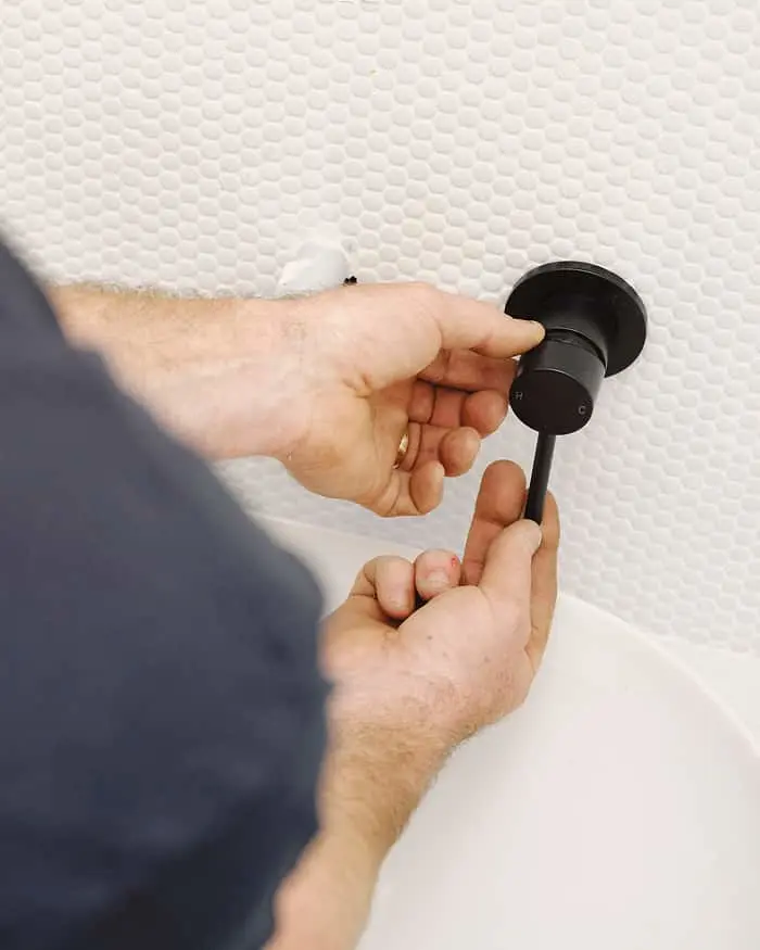 Hands installing a black wall fixture or hook onto a textured white wall.
