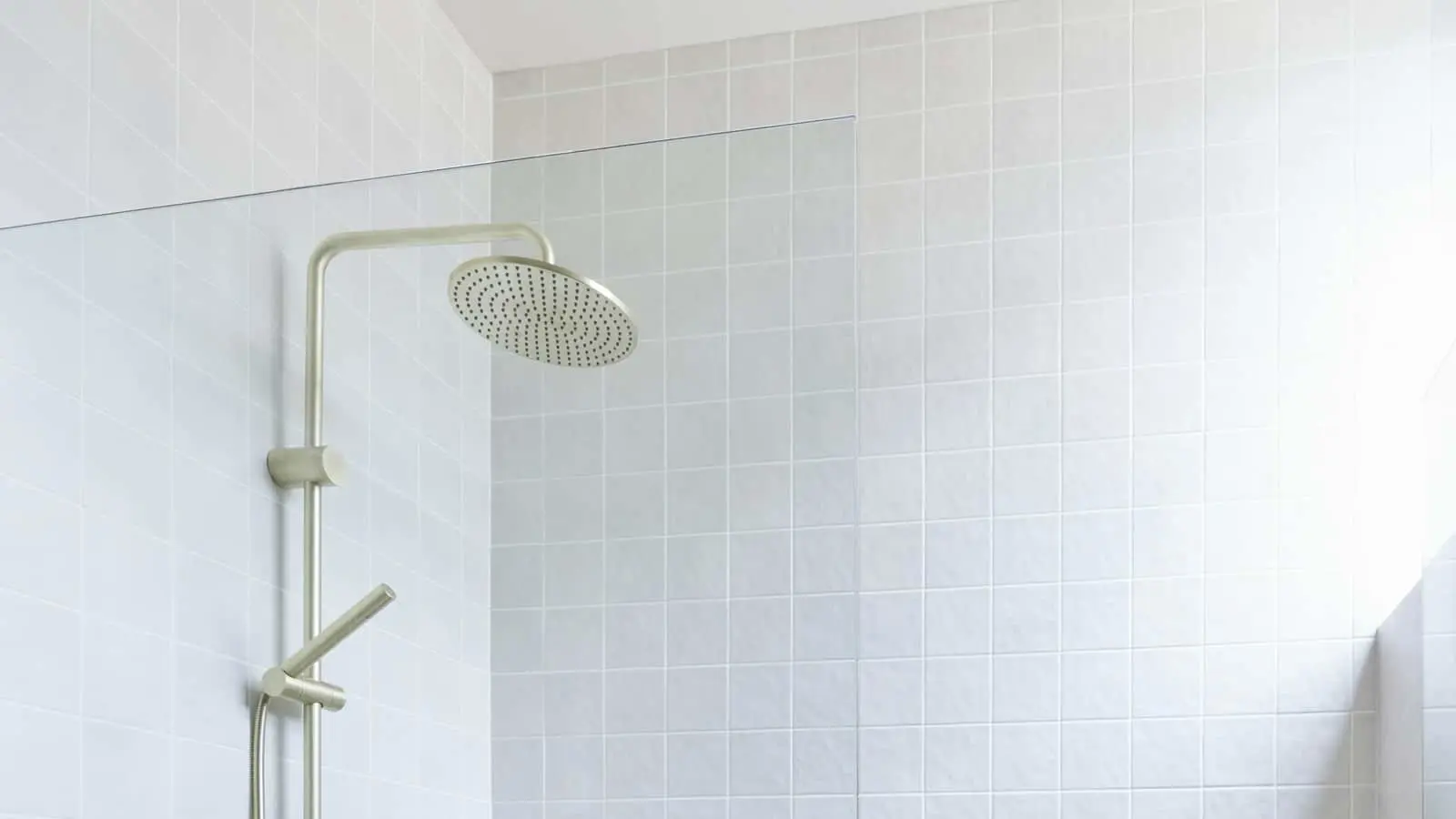 Modern shower with round rainfall showerhead mounted on brushed metal fixture in a light-tiled bathroom.