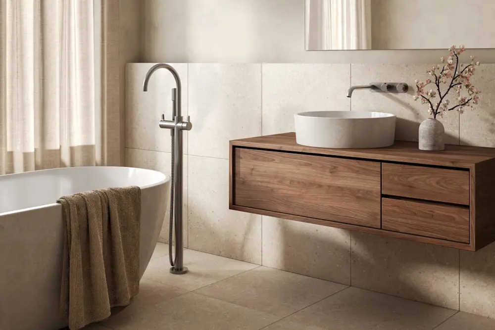 Bathroom with a white freestanding tub, floor-mounted faucet, floating wood vanity, round vessel sink, and a small floral arrangement.