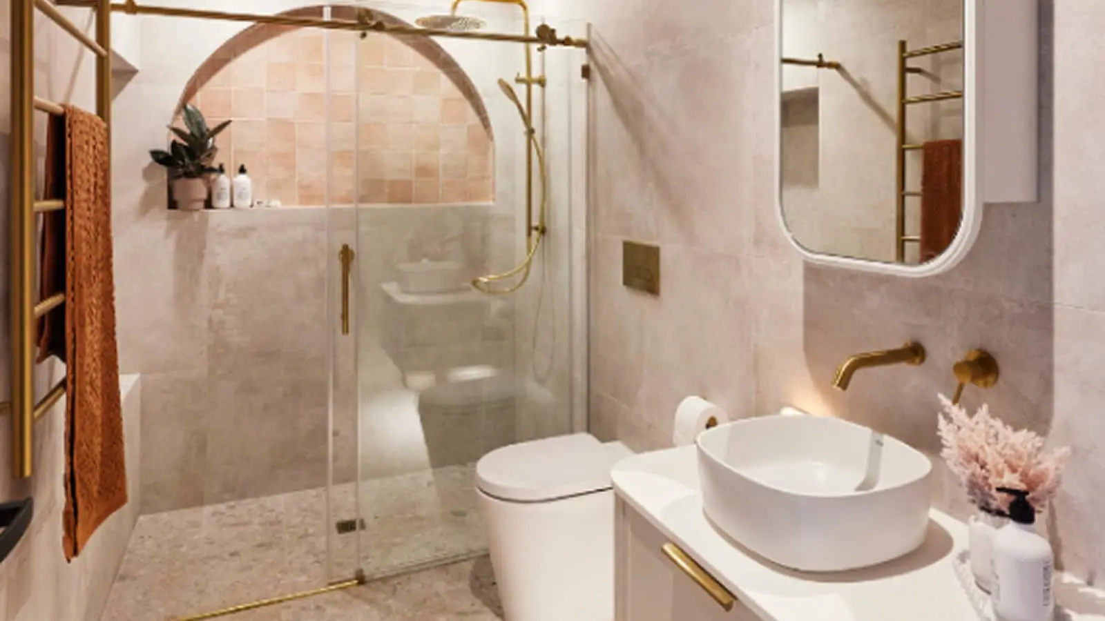 Modern bathroom with pink tile walls, glass shower, white vessel sink, gold fixtures, and decorative plants.