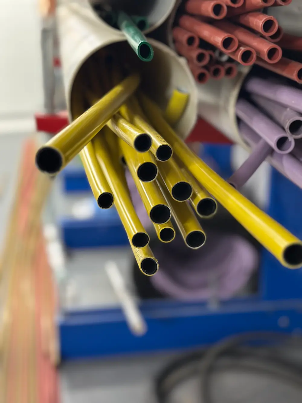Colorful plastic pipes in yellow, green, red, and purple organized in bundles, with yellow tubes prominently displayed in front.