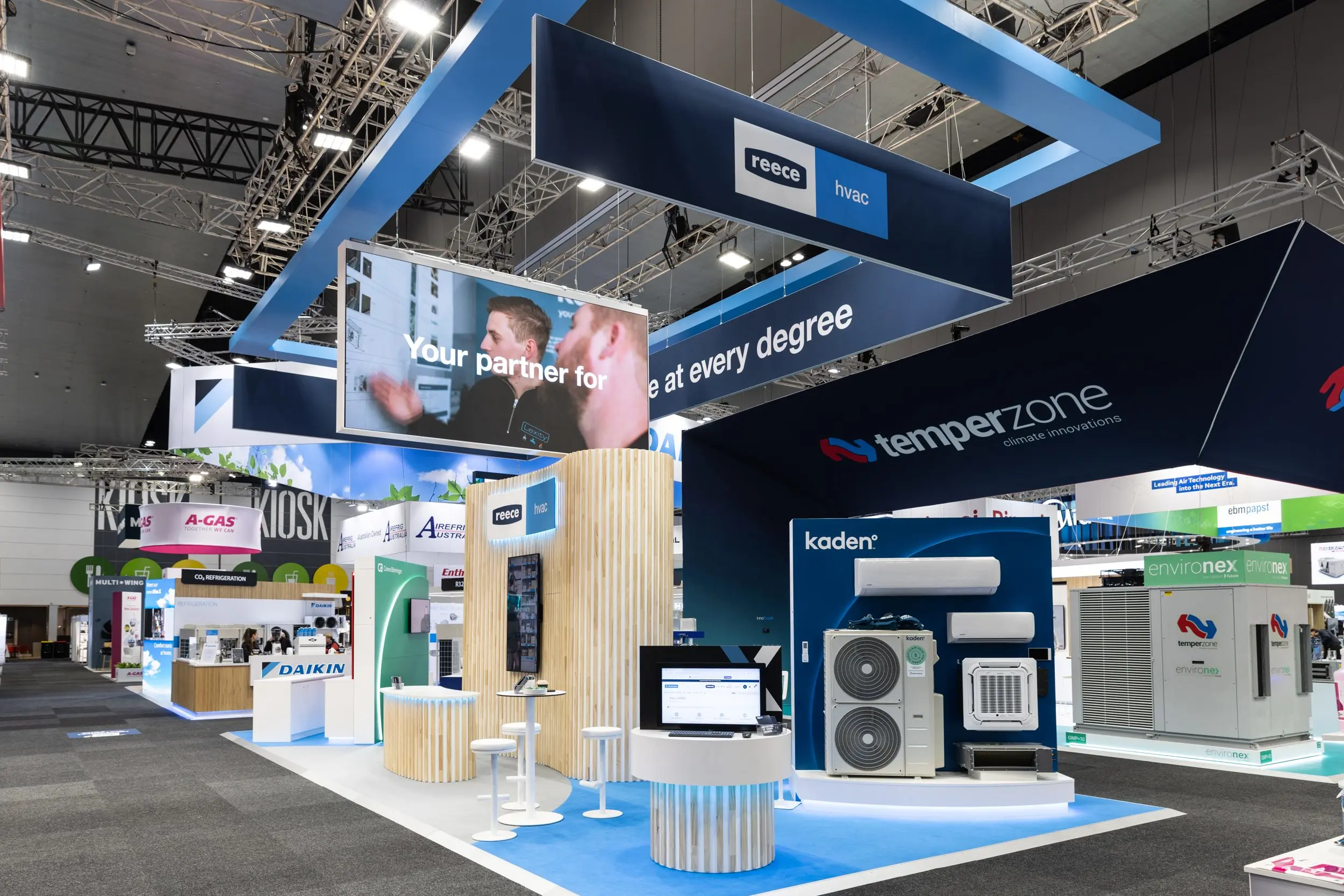 Reece HVAC trade show booth displaying Temperzone and Kaden air conditioning units, with signage and screens in a large exhibition hall.