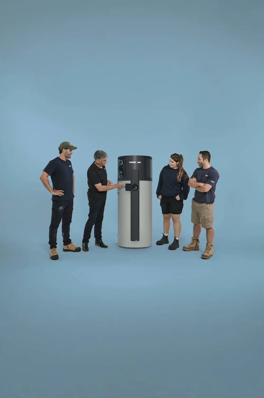 Four people in work attire gathered around a cylindrical Thermann water heater against a blue background.