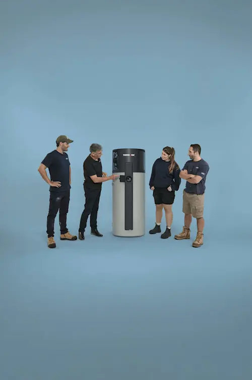 Four people in work attire gathered around a cylindrical Thermann water heater against a blue background.