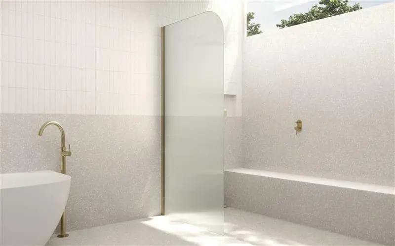 Modern minimalist bathroom with white tiled walls, glass shower partition, gold fixtures, and natural light from above.