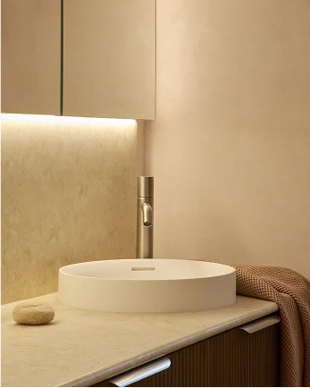 Modern bathroom vanity with white circular sink, chrome faucet, and warm beige walls with subtle lighting.