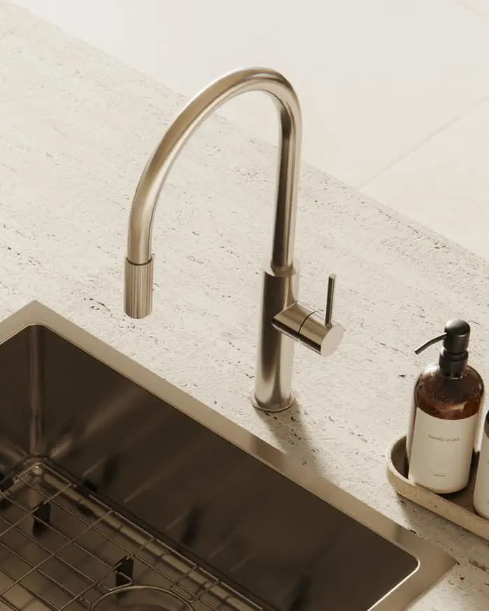 A brushed nickel pull-down kitchen faucet on a stone countertop beside a stainless steel sink and a hand soap dispenser.