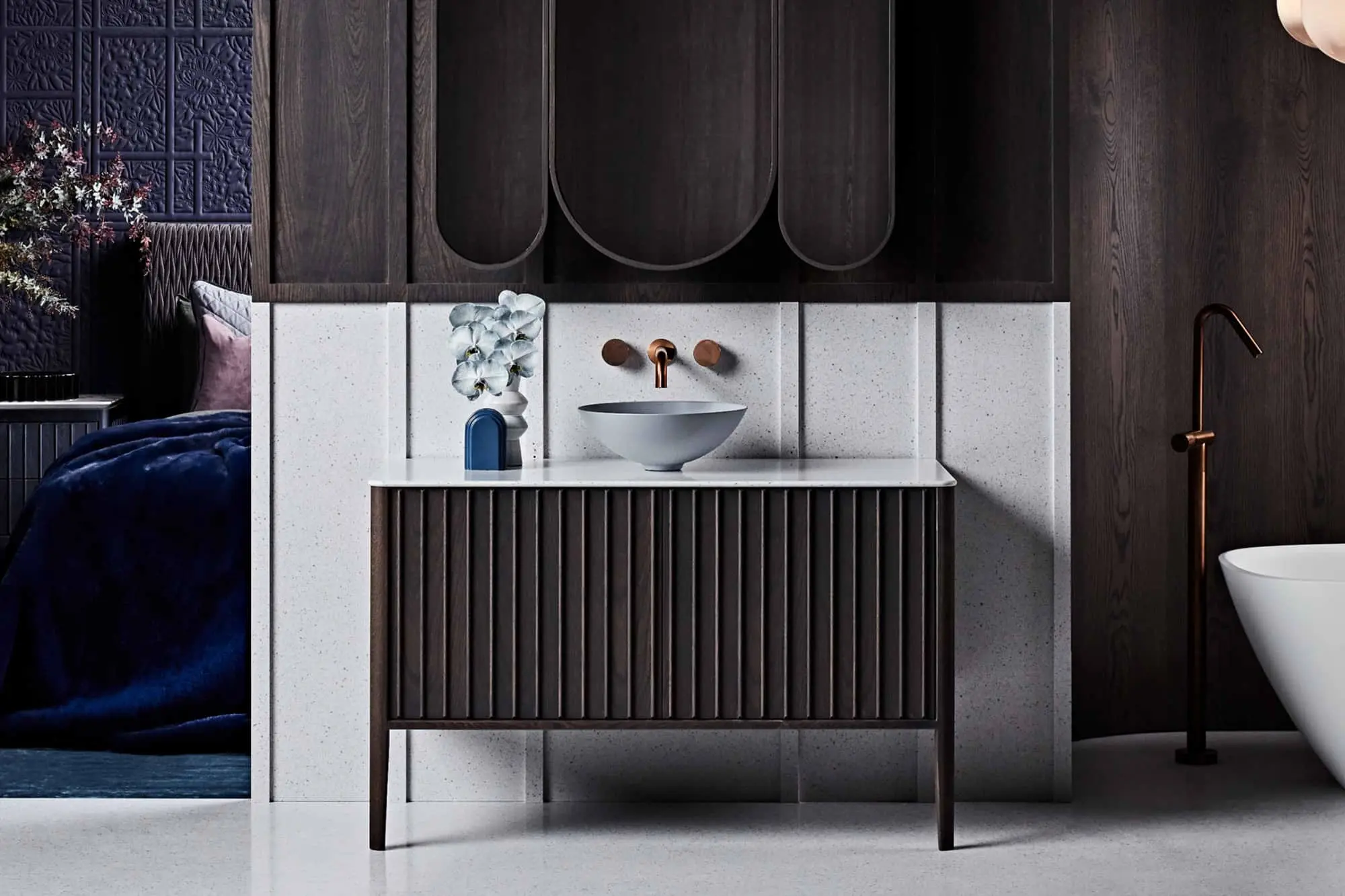 Modern bathroom with dark wood vanity, white bowl sink, copper fixtures, and blue textured wall panels.
