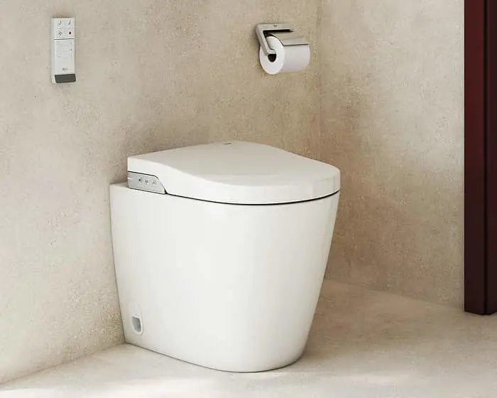 Modern white toilet with electronic control panel mounted on beige wall, toilet paper holder visible above.
