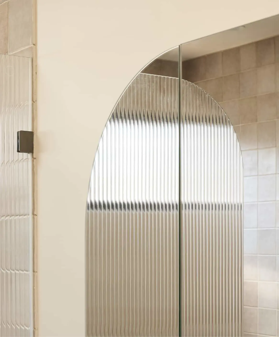 Modern bathroom with arched ribbed glass door panel against beige tiled walls.