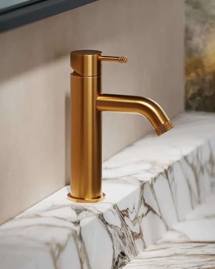 Modern gold bathroom faucet with textured handle and spout mounted on white marble countertop with gray veining.