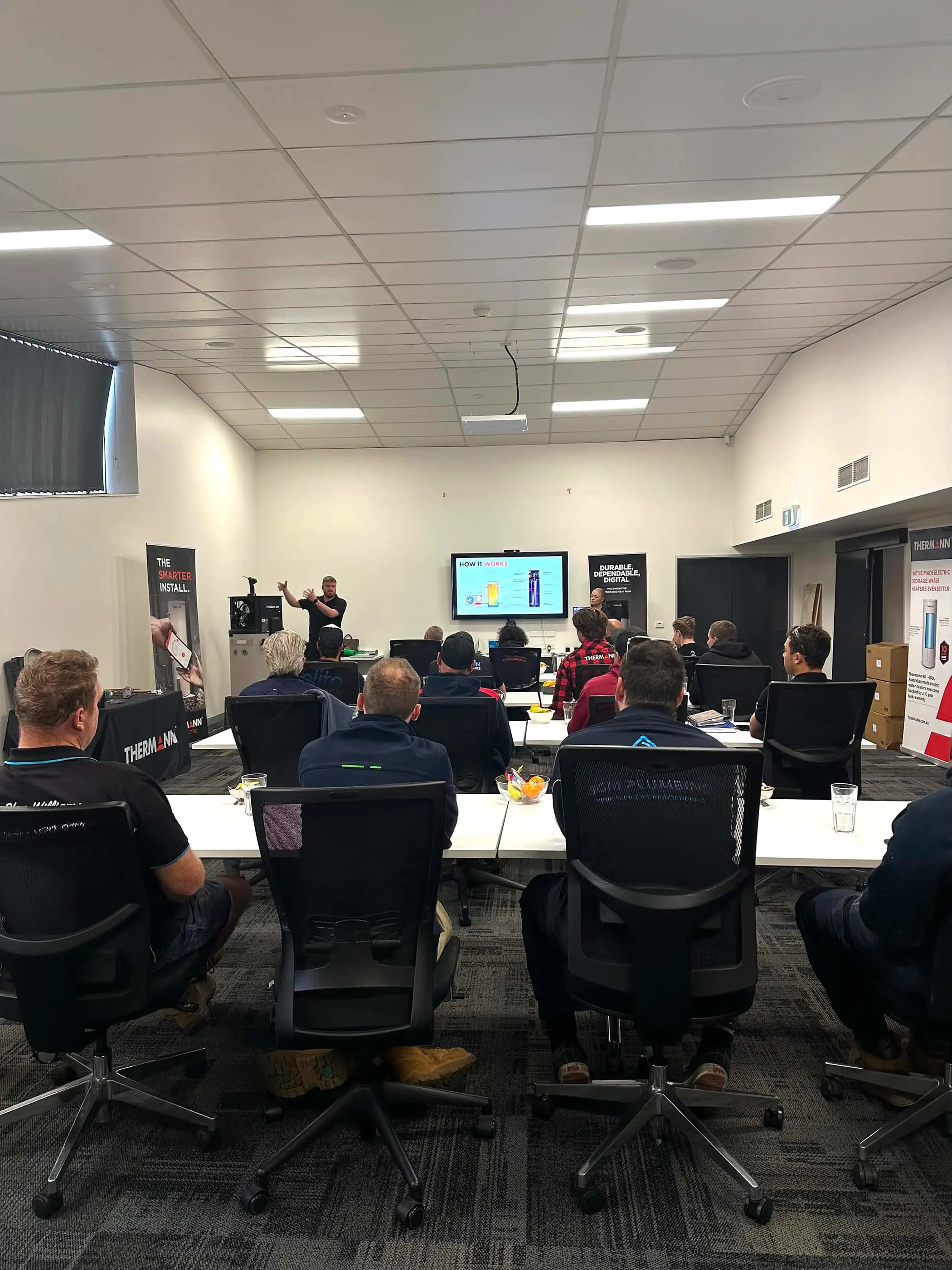 Training session with attendees seated at tables facing presenter and screen displaying product information.