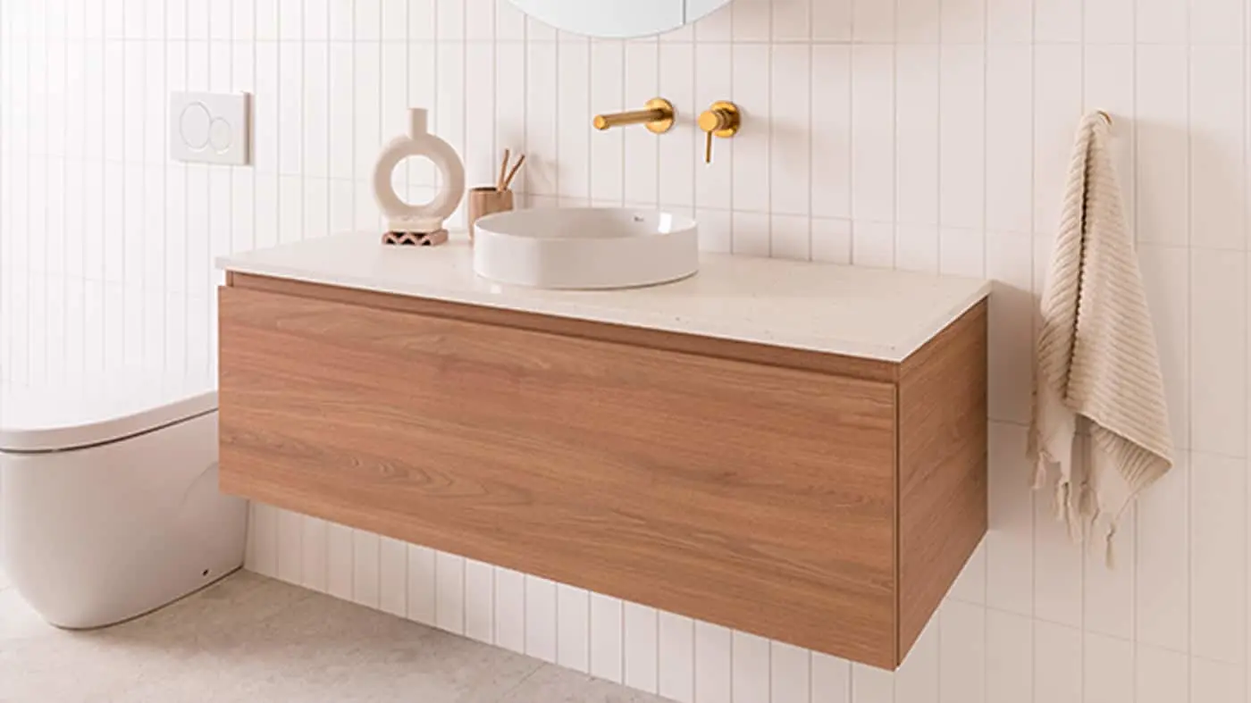 Modern bathroom with wooden floating vanity, white vessel sink, gold wall-mounted faucet, and beige towel hanging nearby.
