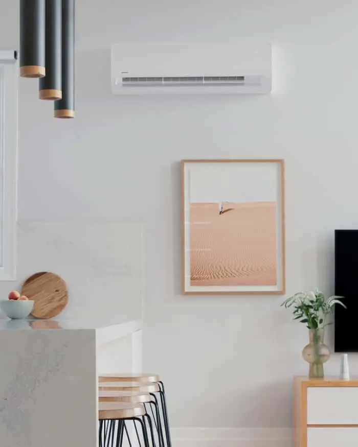 Modern minimalist room with wall-mounted air conditioner, desert artwork, pendant lights, and marble countertop.