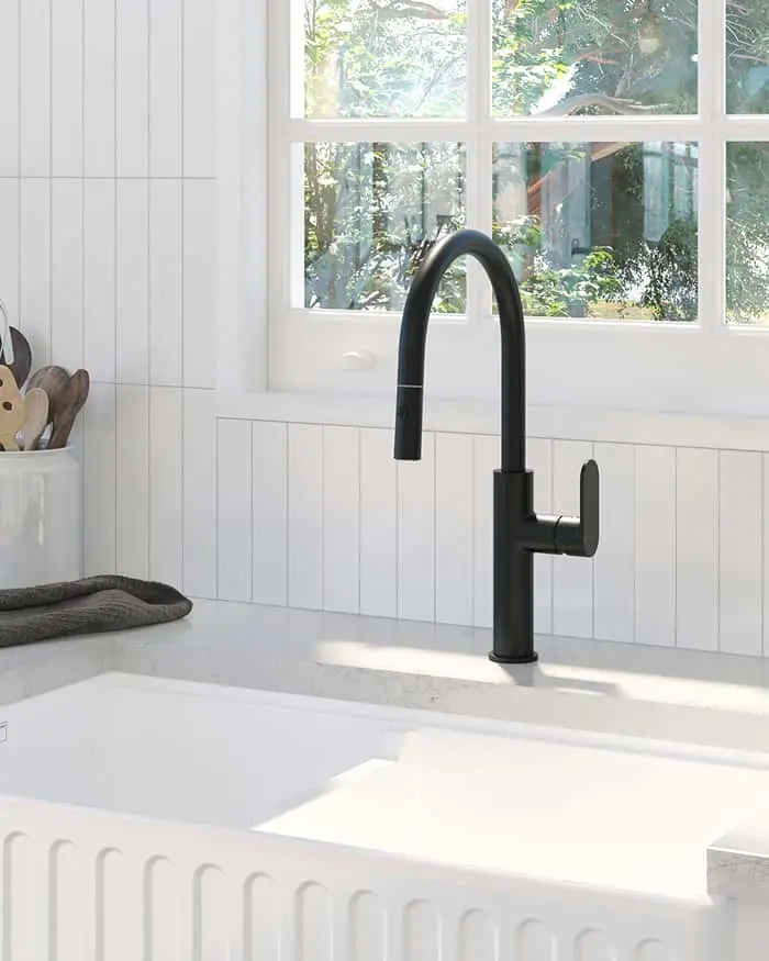 Modern black faucet over white farmhouse sink with window overlooking greenery and wooden utensils nearby.