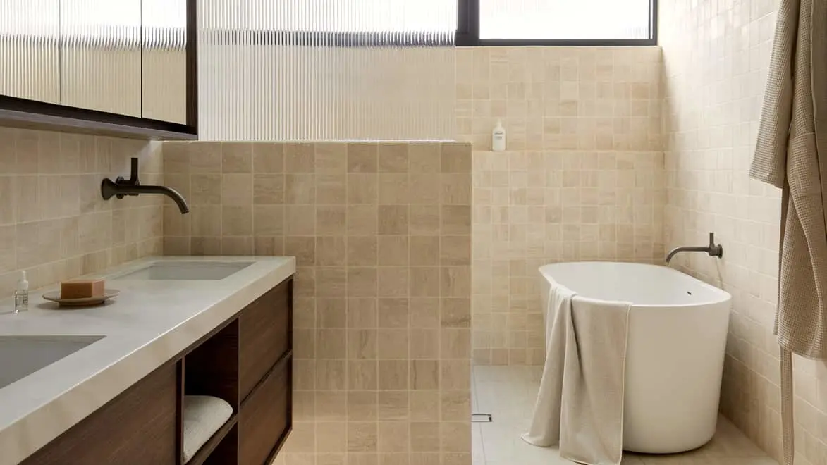 Modern bathroom with beige tile walls, white freestanding tub, dark wood vanity, and minimalist fixtures.