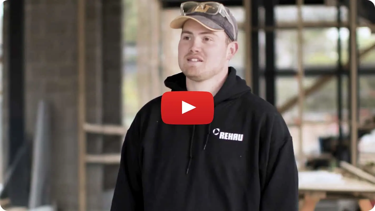 Person in cap and REHAU hoodie with YouTube play button overlay, standing in construction setting.