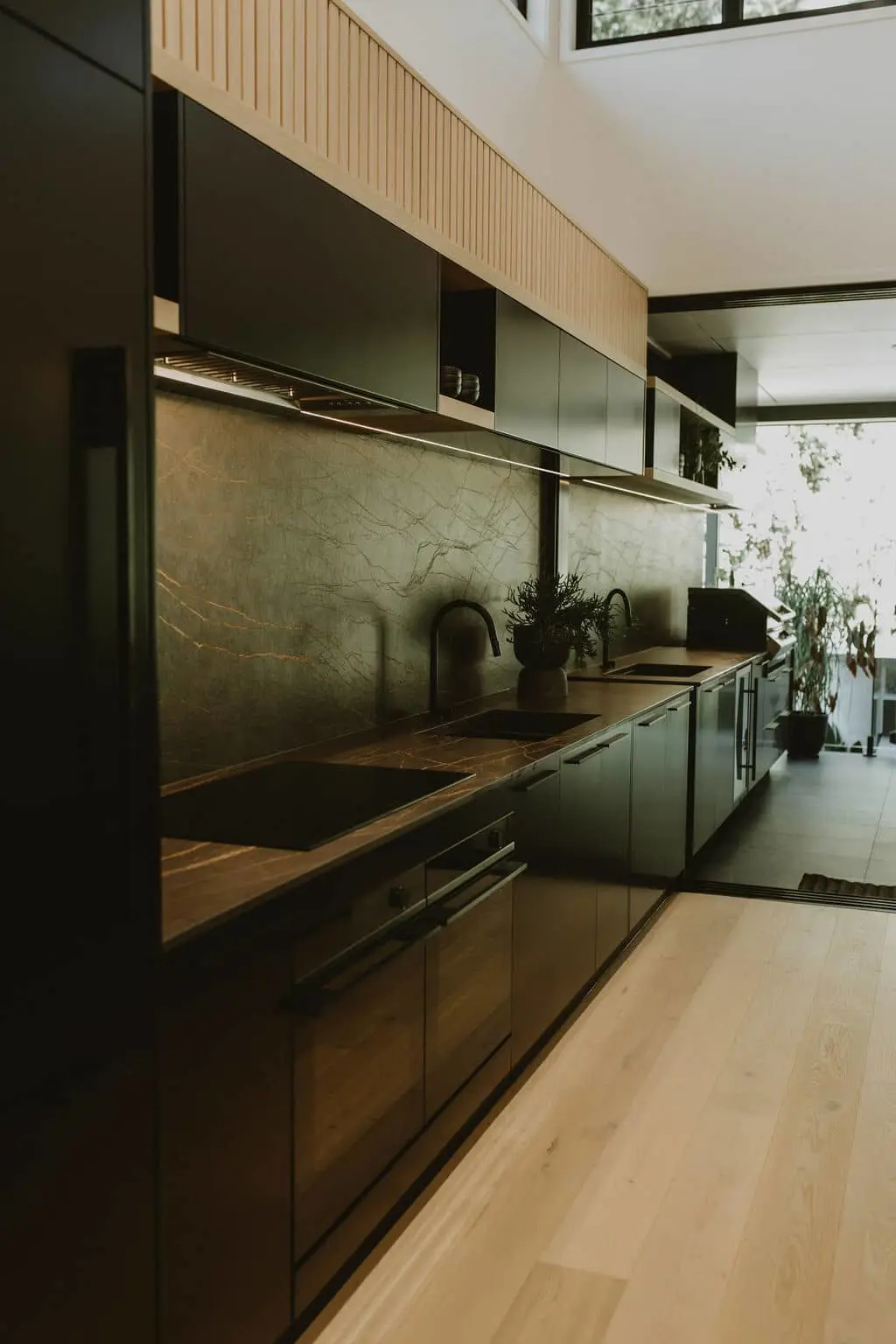 Modern kitchen with black cabinets, wooden countertops, marble backsplash, and natural light from nearby windows.