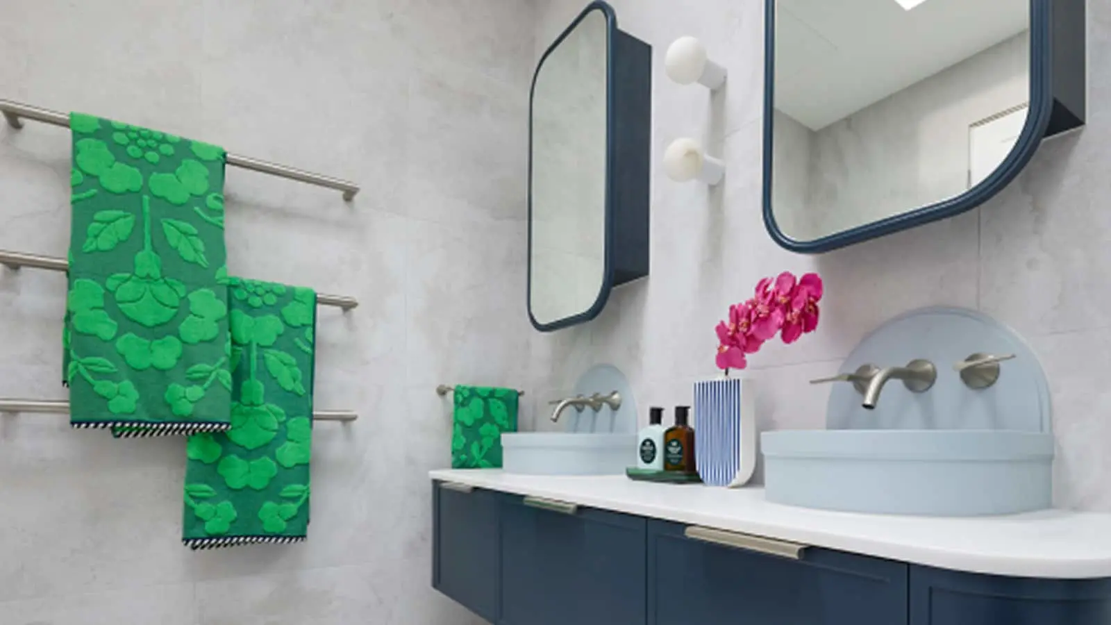 Modern bathroom with blue vanity, white sinks, green floral towels, and pink flowers in a striped vase.