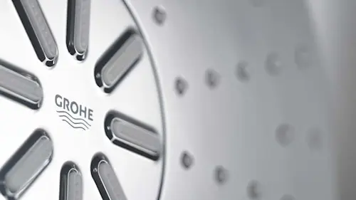 Close-up of a GROHE shower head with metal spray nozzles arranged in a circular pattern.