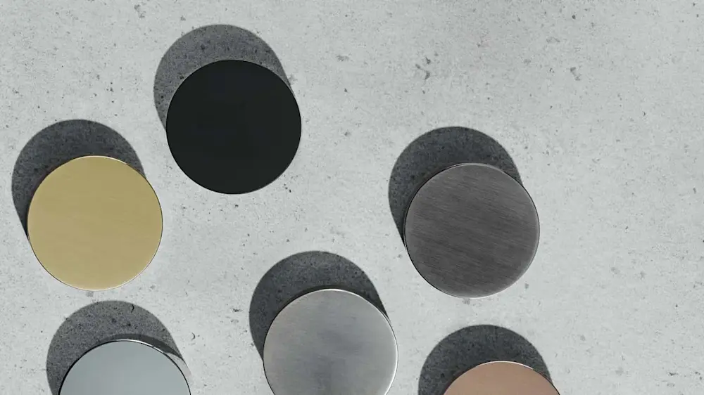 Six circular metal discs in different finishes including gold, black, and silver arranged on a light gray textured surface.