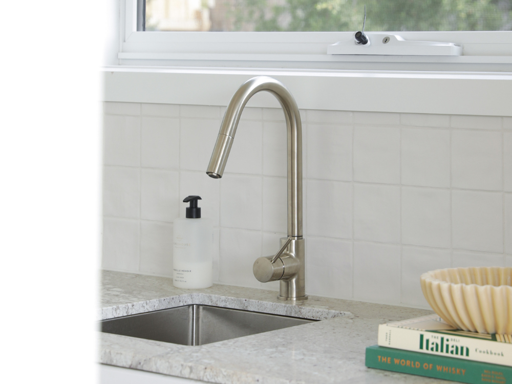 Modern kitchen sink with brushed nickel faucet, white tile backsplash, marble countertop, and cookbooks nearby.