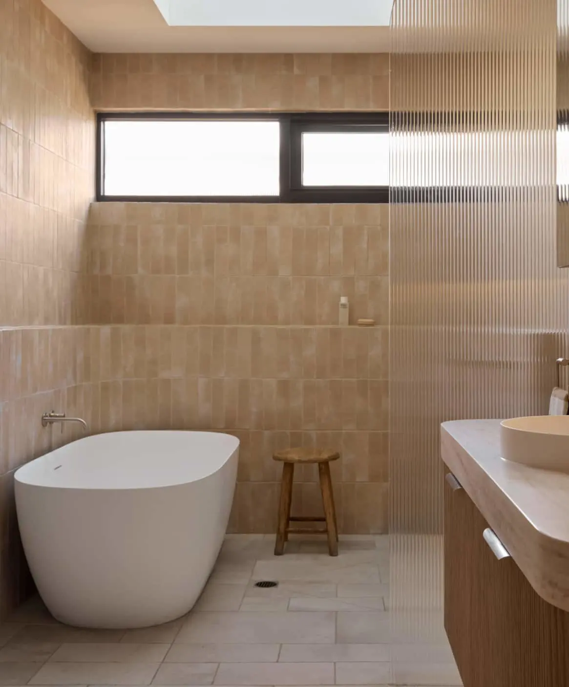 Modern bathroom with beige tiles featuring a freestanding tub and skylight.