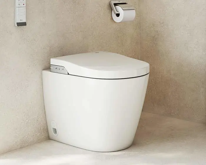 Modern white toilet with closed lid against beige walls, with toilet paper holder mounted nearby.