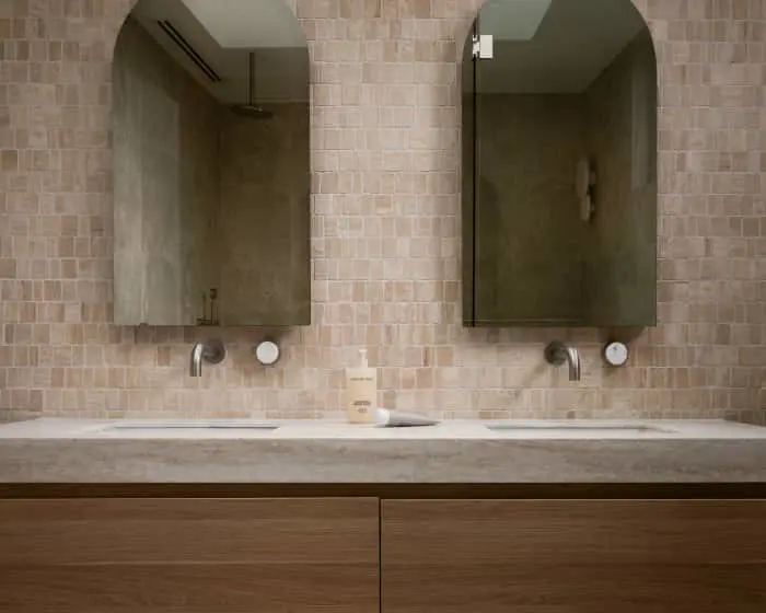 Modern bathroom with two arched mirrors above a concrete countertop with wall-mounted faucets and beige tile wall.