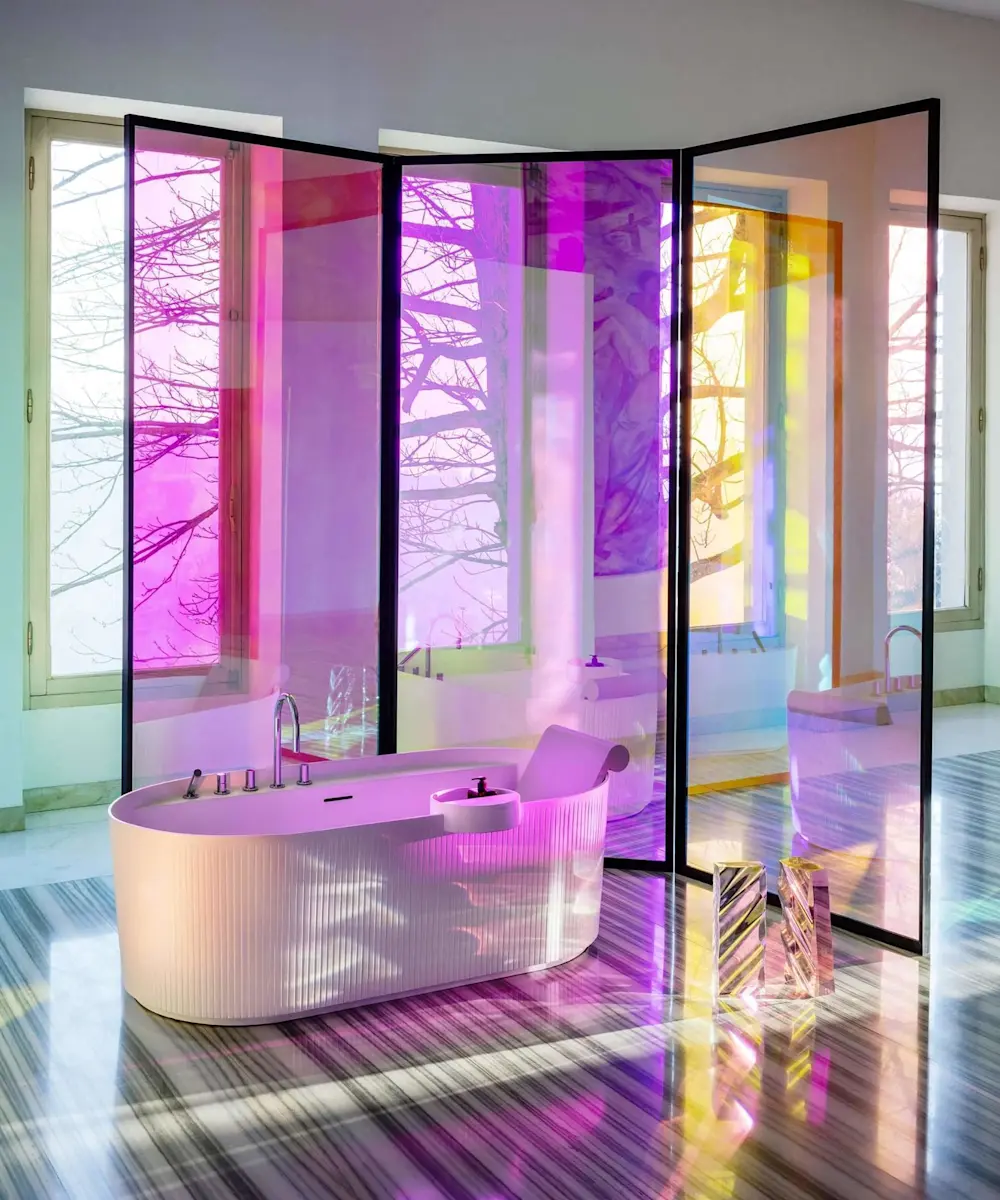 Modern bathroom with white bathtub illuminated by colorful purple and yellow light filtering through glass panels.