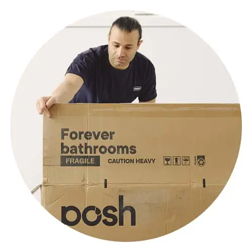 Person in navy shirt handling a large cardboard box labeled "Forever bathrooms" and "posh" with shipping warnings.