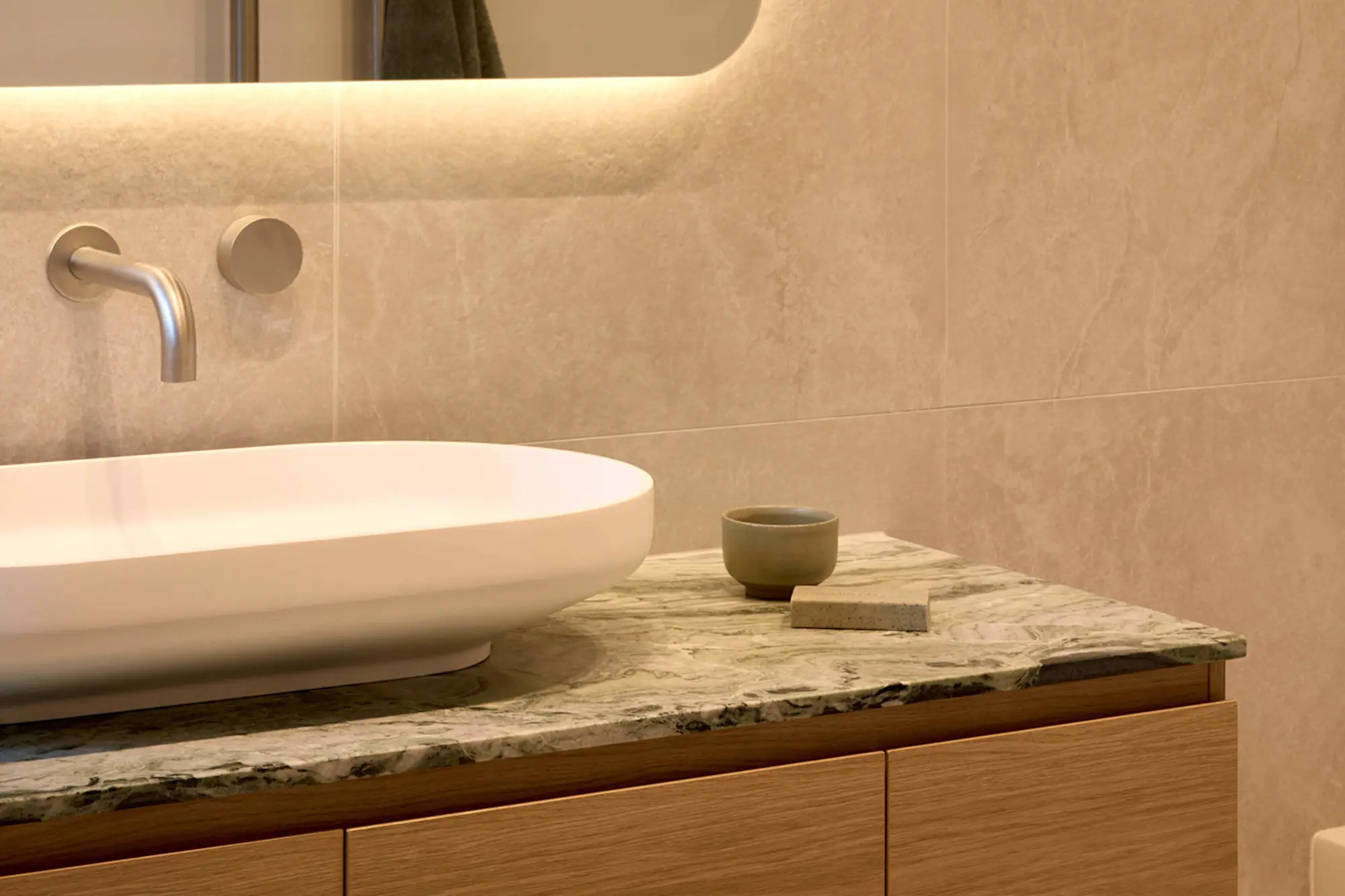 Modern bathroom with white vessel sink on marble countertop, wall-mounted faucet, and beige tiled wall with mirror.