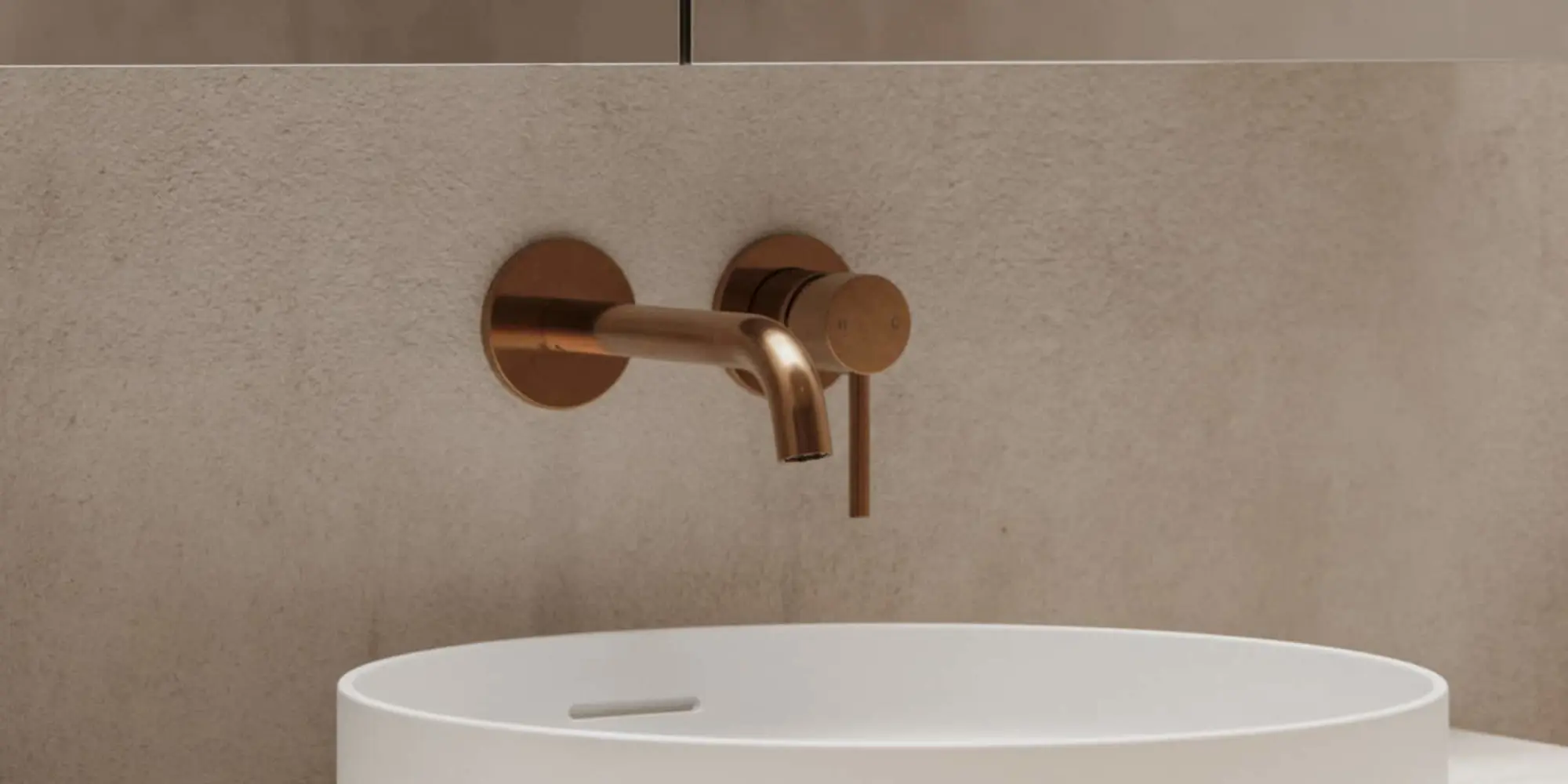 Modern copper wall-mounted faucet above a white basin sink against a beige textured wall.