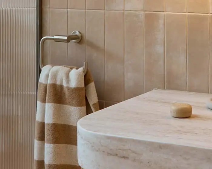 Striped brown and white towel hanging on a metal rack beside a marble countertop in a beige tiled bathroom.