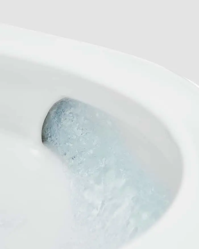 Clear blue water with bubbles flowing in a white porcelain toilet bowl.