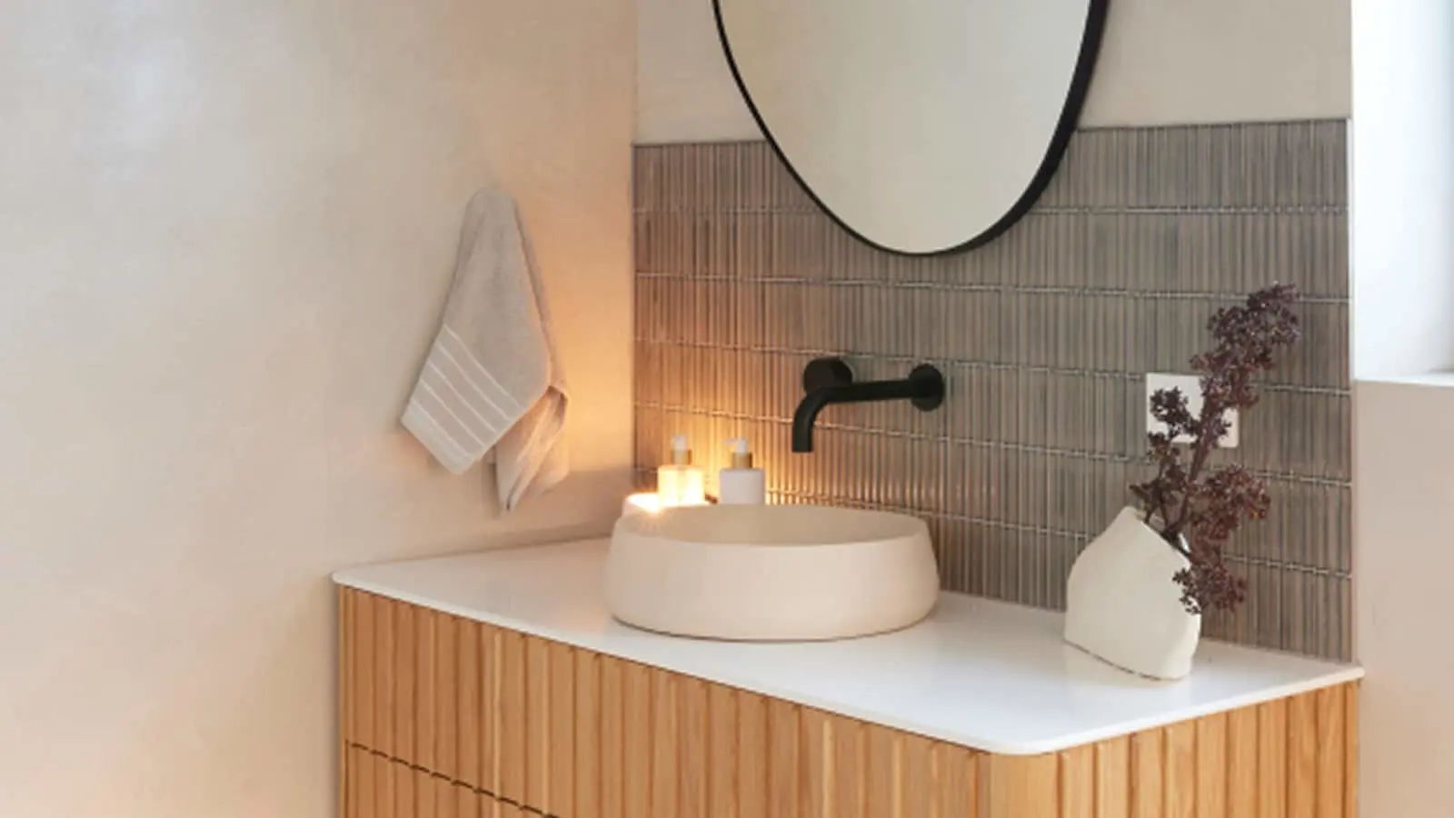 Modern bathroom with round vessel sink, black faucet, wooden vanity, circular mirror, and decorative plants.