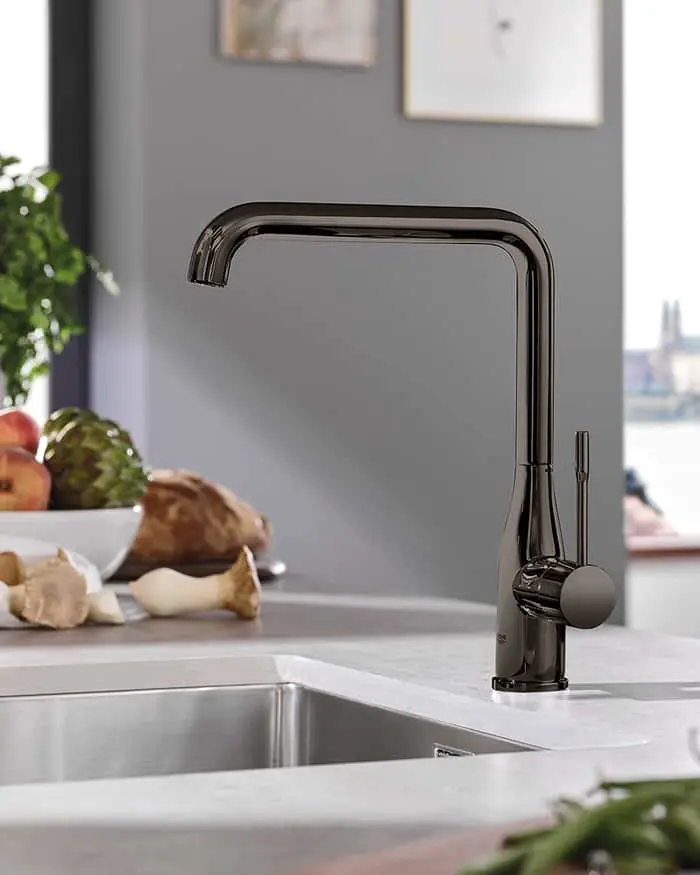 Modern black kitchen faucet with high arch spout on white countertop, sink visible with fresh vegetables nearby.