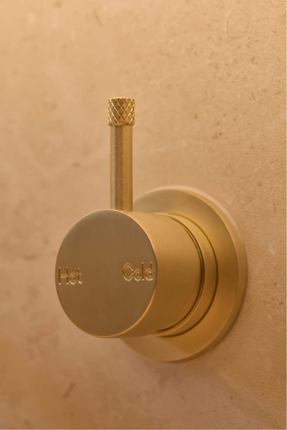 Brass wall-mounted faucet with textured knurled handle and circular dial labeled Hot and Cold on beige wall