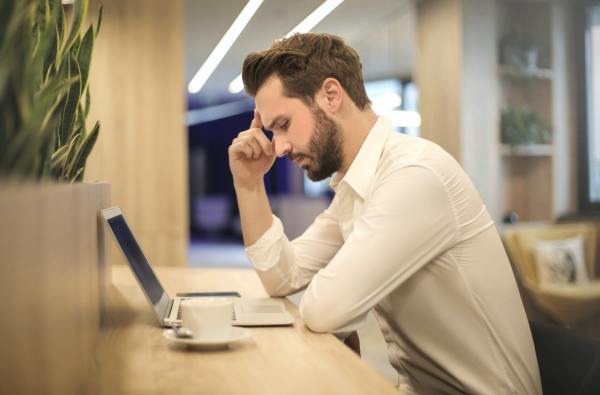 A young white man frowns at his laptop keyboard, perhaps contemplating the existential ramifications of late-stage capitalism