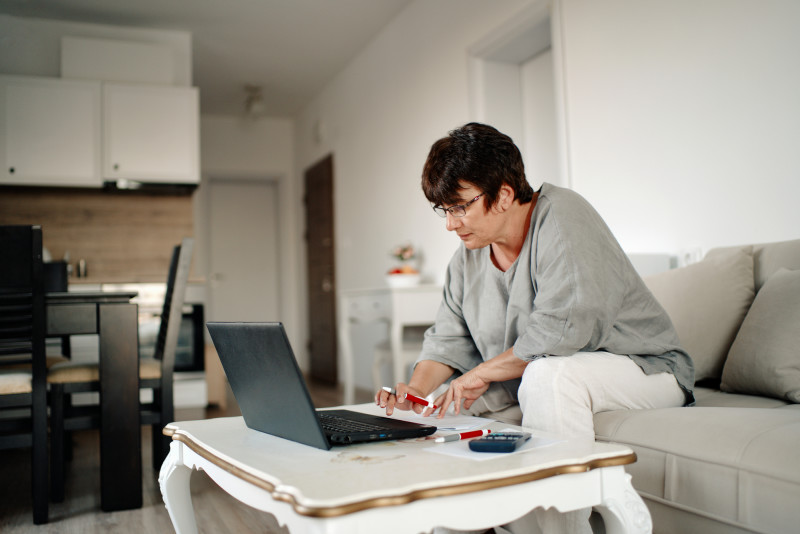 Older woman sitting on a couch looking at a laptop