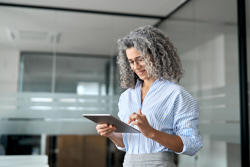 Woman with curly, grey hair wearing a striped shirt and looking at a tablet